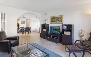 A modern living room with a glass coffee table, leather sofa, and entertainment unit with a flat-screen TV.