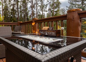 Mesa al aire libre con superficie de vidrio, un letrero que dice "S'mores Station" y una chimenea al fondo.