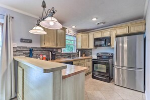 A modern kitchen with wooden cabinets, stainless steel appliances, a central island, and a hanging light fixture. - 5 Mi to Fort Hood! ‘Brooklyn House’ w/ Fenced Yard (Killeen)