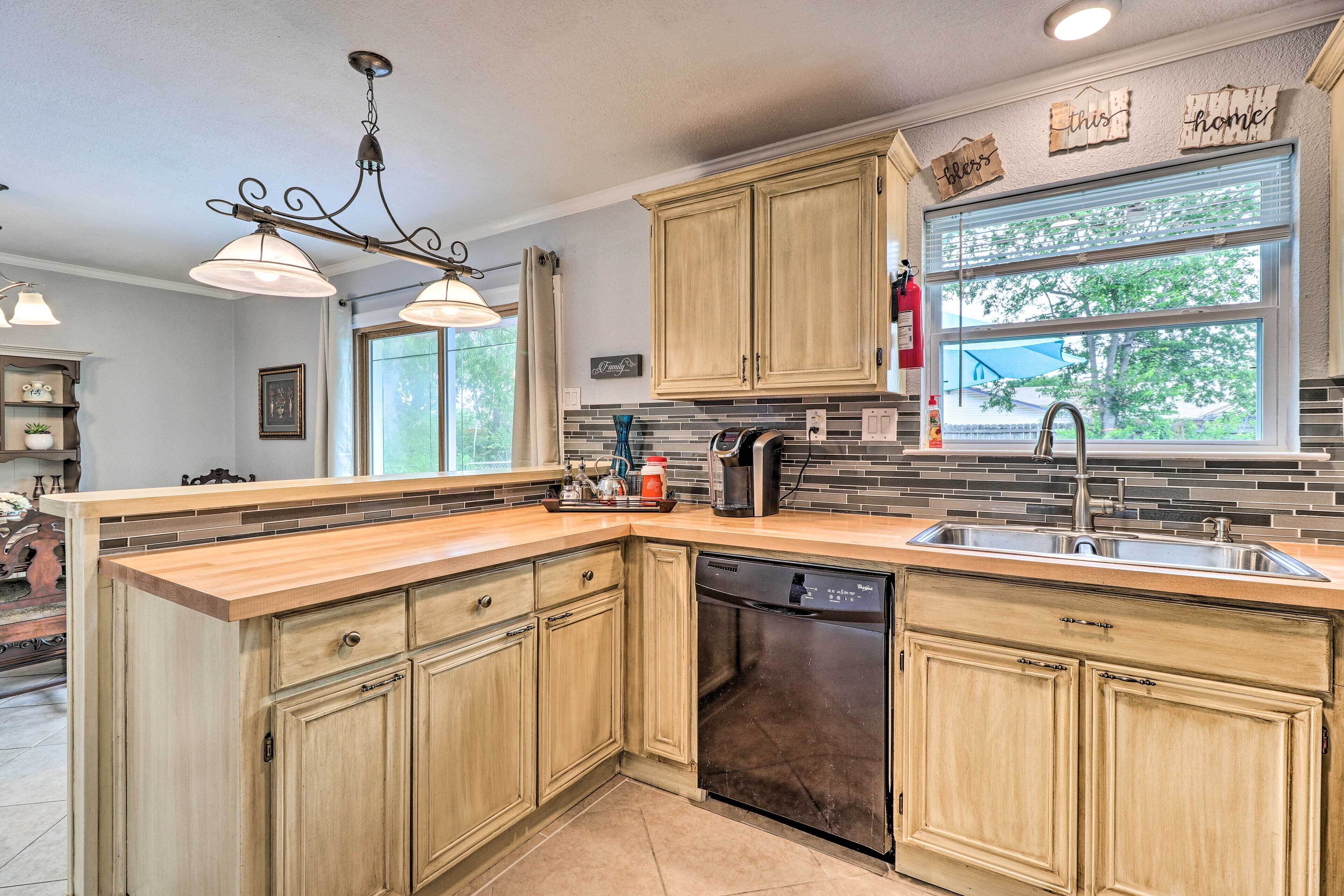 A kitchen with wooden cabinets, a dishwasher, a coffee maker, and a window with a view of trees.