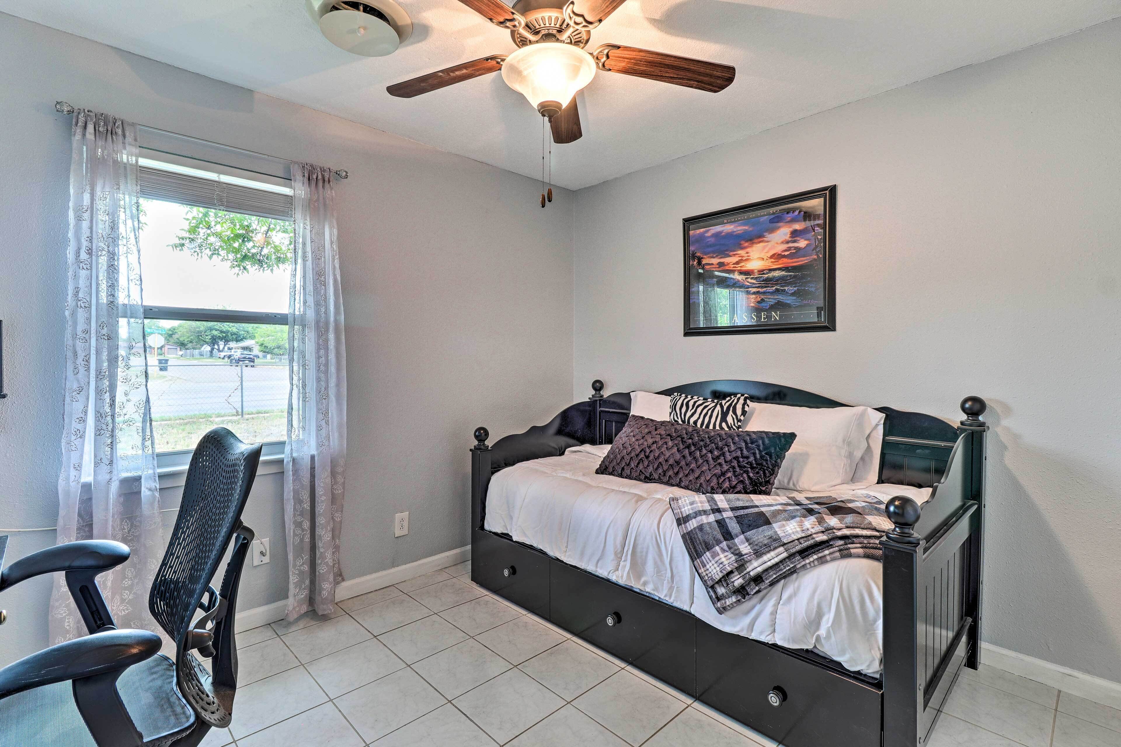 A bedroom with a bed, a ceiling fan, a window with curtains, a chair, and a framed picture on the wall.