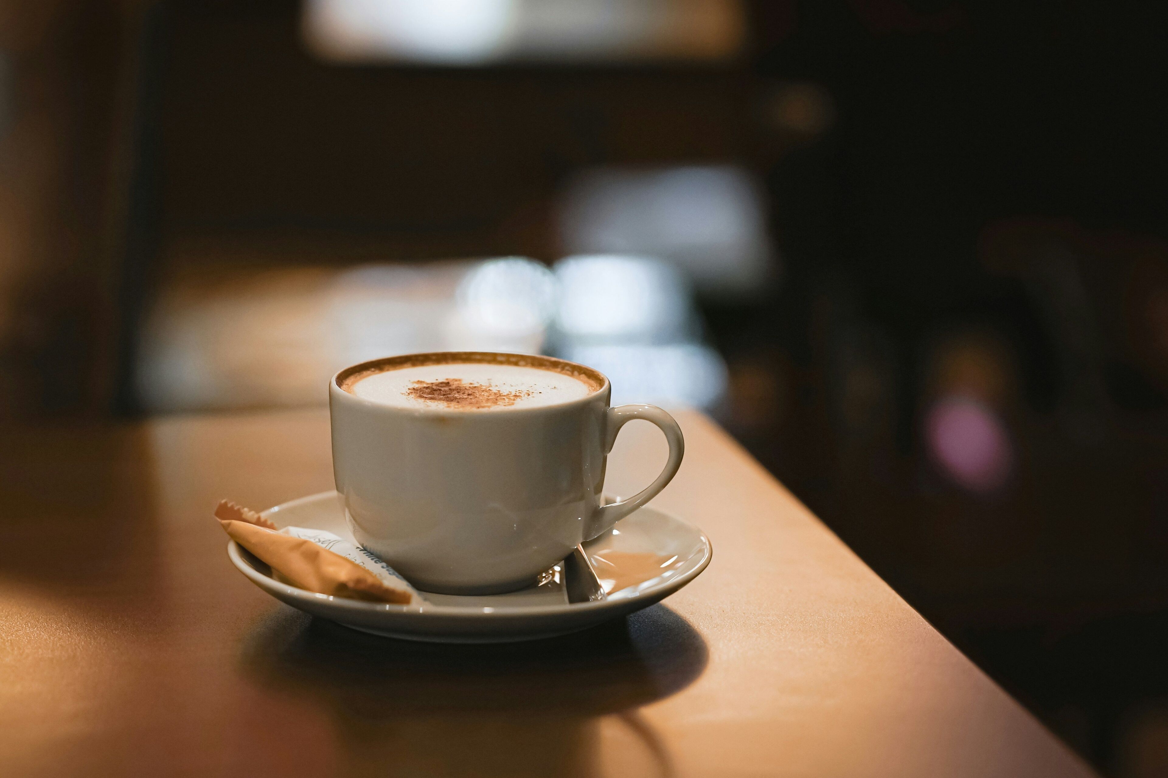 A cup of coffee on a saucer with a biscotti on a small plate, placed on a wooden table.