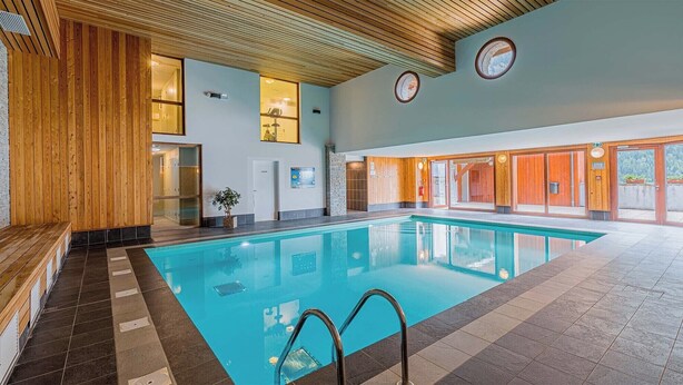 An indoor swimming pool with wooden paneling, a tiled floor, and a bench along the left side.