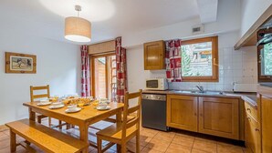 A cozy kitchen with wooden cabinets, a dining table set for breakfast, and a window with curtains.