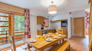 A cozy kitchen with wooden cabinets, a dining table set for breakfast, and a view of greenery outside.