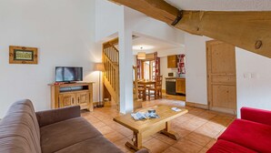 A cozy living room with a sofa, a wooden coffee table, and a TV. There is a staircase leading to another room.