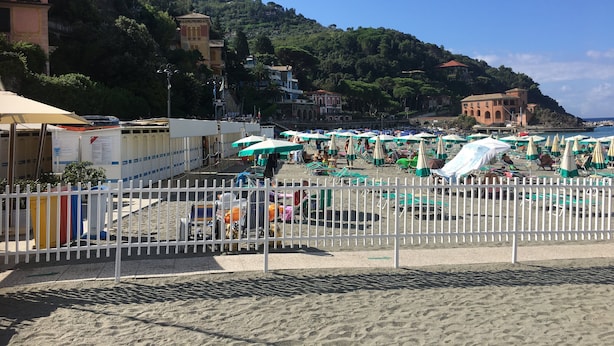 A beach with umbrellas and sun loungers, a white fence, and buildings in the background. - 1 Bed Studio - Pets - Terrace - Parking (Borgo Val di Taro)