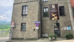 A stone building with multiple windows, a banner advertising a museum, and directional signs. - 1 Bed Studio - Pets - Terrace - Parking (Borgo Val di Taro)