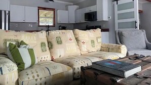 A living room with a sofa, a chair, a coffee table, and a kitchen area in the background. - Stylish, comfortable, and private Guest House. (Eastman)