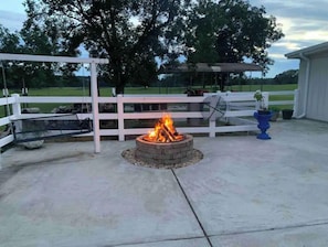 Relax by the fire pit in a serene outdoor setting surrounded by lush greenery and a covered seating area.