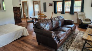 Uma sala de estar com um sofá de couro marrom, uma mesa de jantar de madeira e um ventilador de teto.