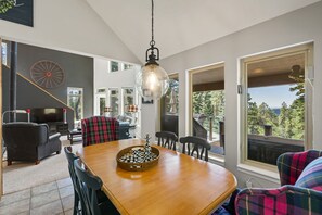 A dining area with a wooden table, chairs, and a chandelier. There is a television and a fireplace in the background. - Pet Friendly, Solitude, 15 Mins to Vallecito! (Bayfield)