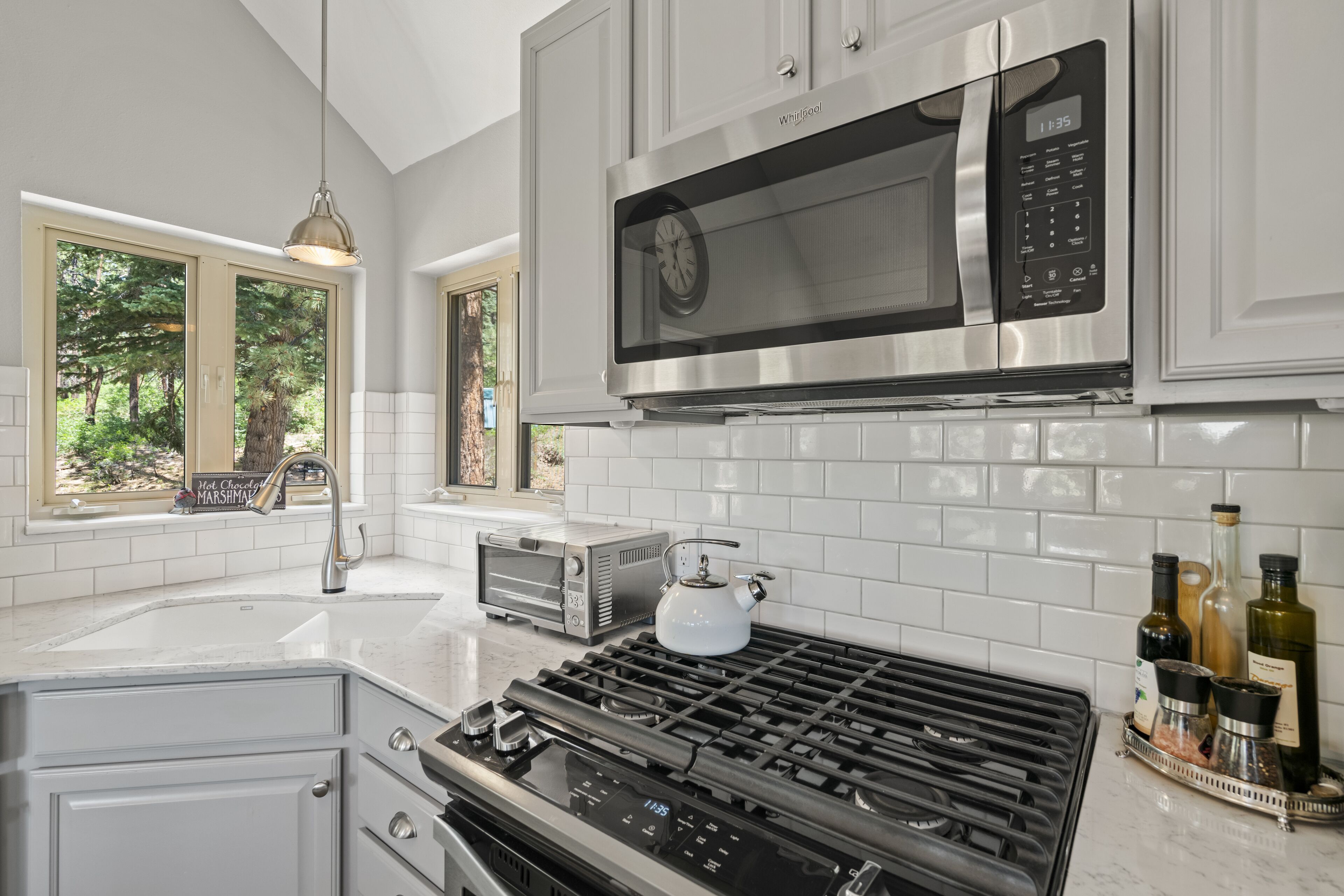 A modern kitchen with white cabinets, a stainless steel microwave, a gas stove, and a window with a view of trees.