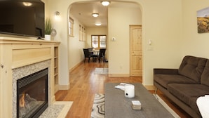 A living room with a fireplace, a flat-screen TV, a brown sofa, and a dining area in the background. - Excellent Location- Downtown Carbondale on Main St.! (Carbondale)