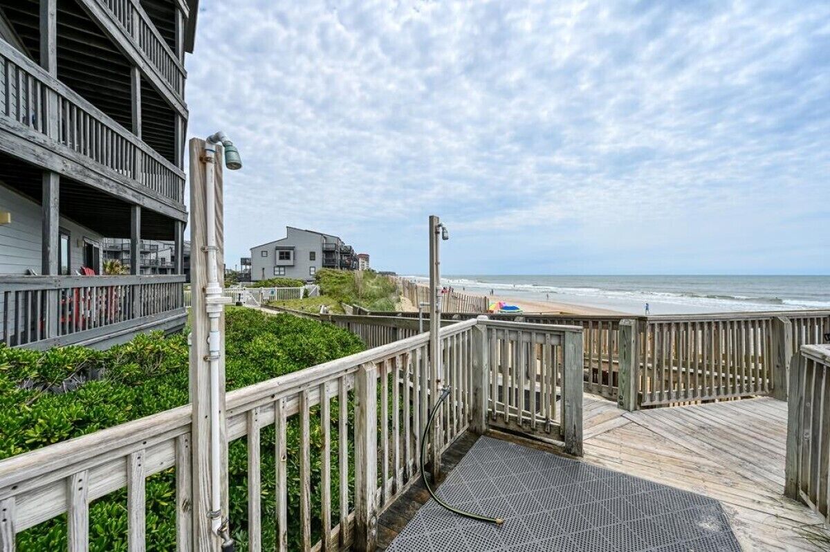 A wooden deck overlooking a beach with a view of the ocean and a building in the background.