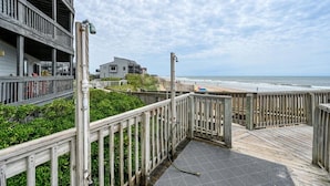 Een houten terras met uitzicht op een strand en de oceaan, met een gebouw op de achtergrond.
