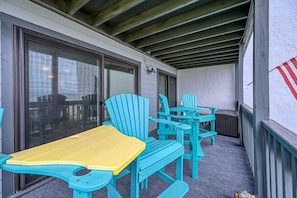 An outdoor seating area with turquoise and yellow chairs and a table, a covered patio with a wooden ceiling, and a white wall with a red and white striped flag.