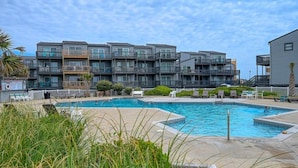 Een modern appartementencomplex met een zwembadgedeelte, inclusief ligbedden en een klein terras.