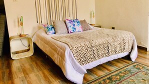 A bedroom with a bed, pillows, a bedside table, a lamp, and a patterned rug. - Junior Suite Mesh View with view of the mountains (Rionegro)