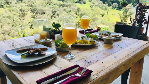 A wooden table set with plates of food, glasses of orange juice, and a small bowl of fruit. - Junior Suite Mesh View with view of the mountains (Rionegro)