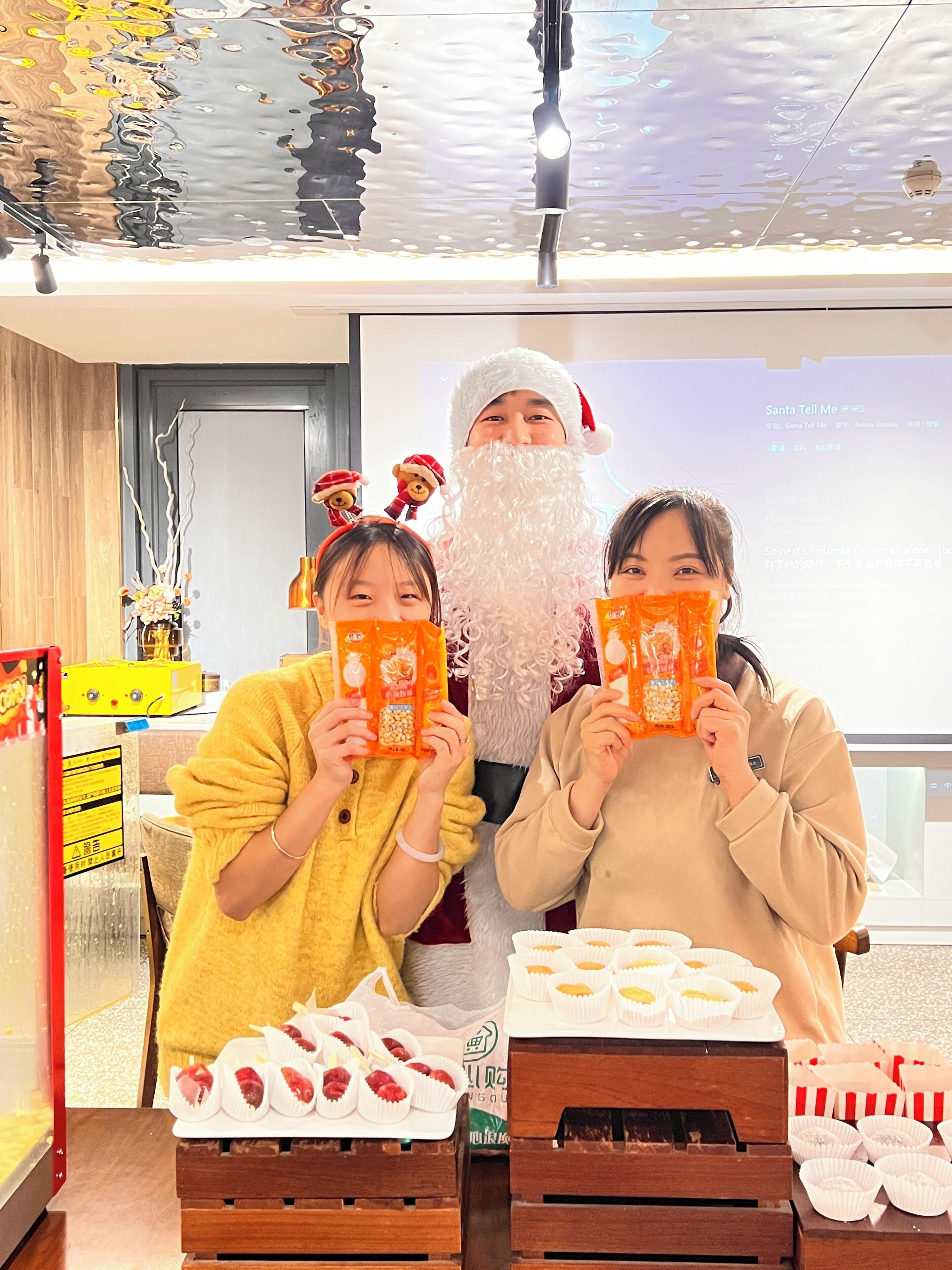 Un grupo de personas en un ambiente interior moderno con techo reflectante, un mueble de madera con alimentos y una pantalla digital al fondo.