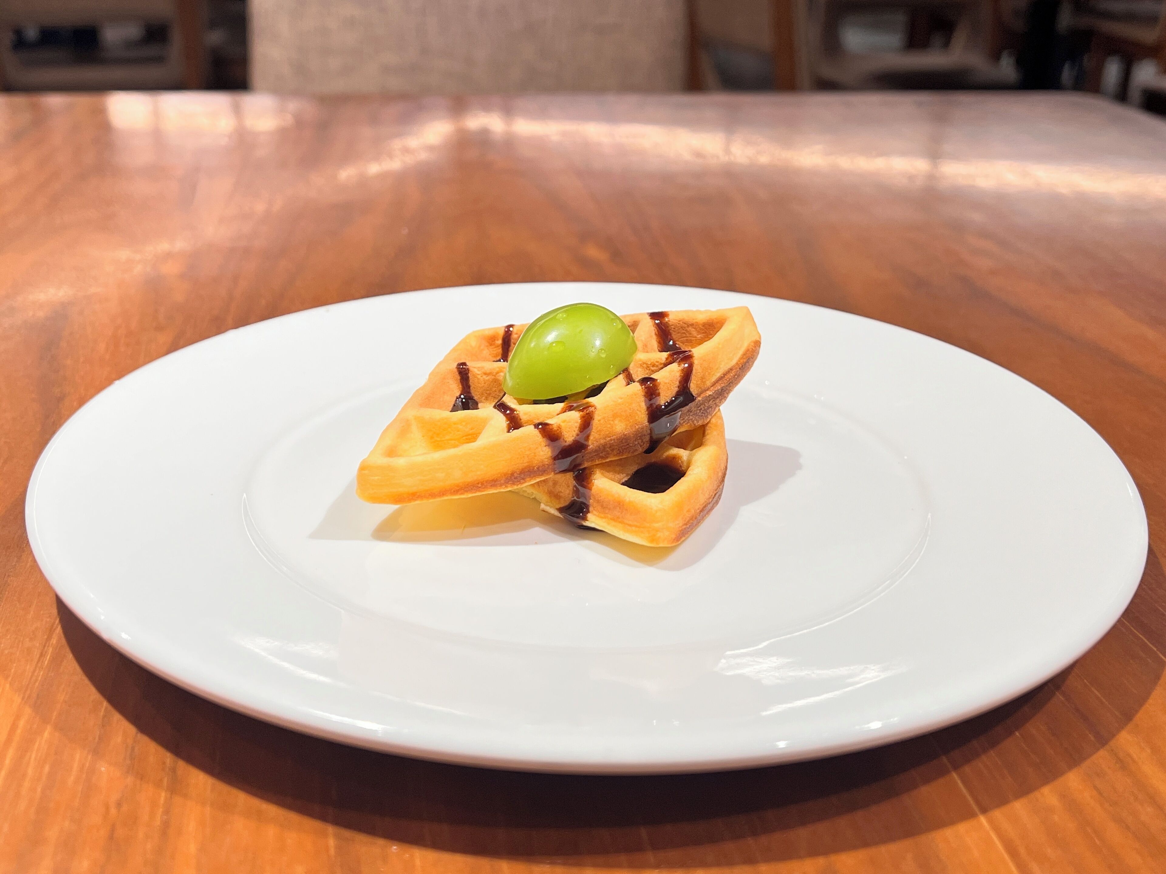 Un waffle con sciroppo e un frutto verde su un piatto bianco su un tavolo di legno.