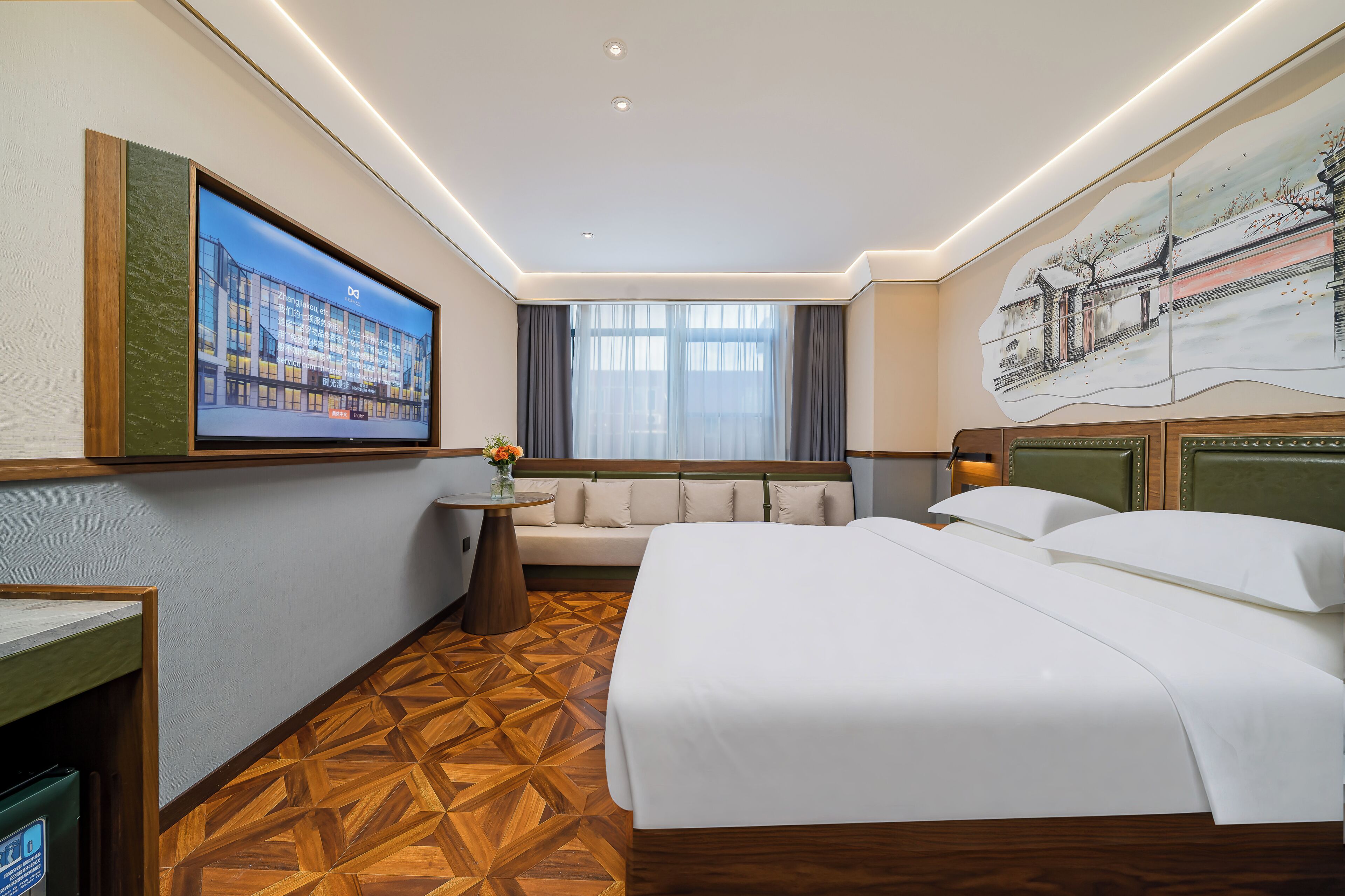 Habitación de hotel con cama, sofá, una mesita con un florero, un cuadro en la pared y una ventana con cortinas.