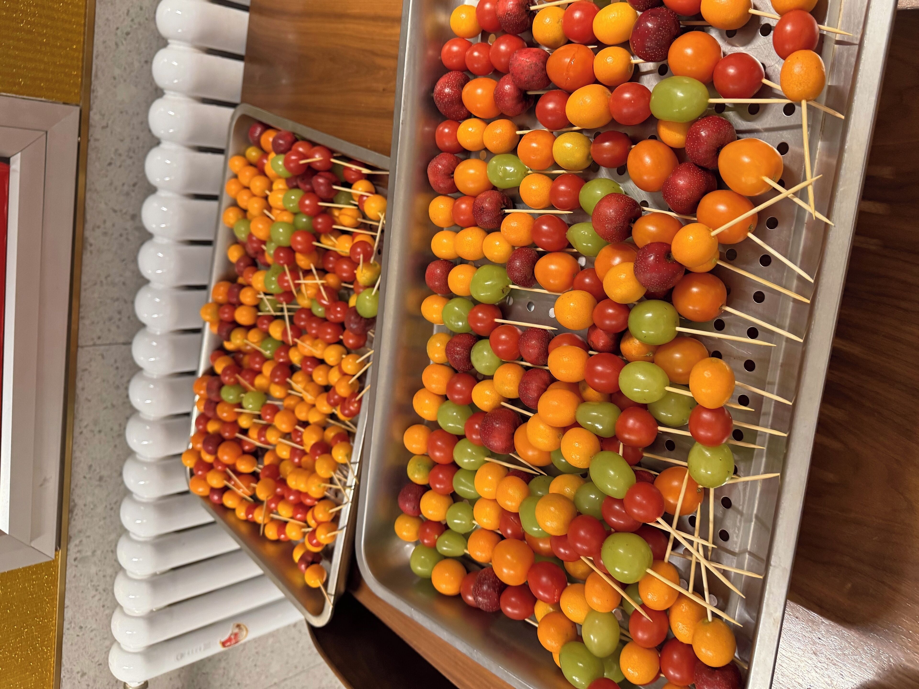 Espetinhos de fruta em diversas cores sobre bandejas.