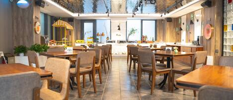 A spacious restaurant with high ceilings, wooden tables and chairs, and large windows.