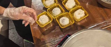Una persona preparando comida, concretamente dumplings, sobre una mesa de madera con diversas herramientas y ingredientes de cocina.