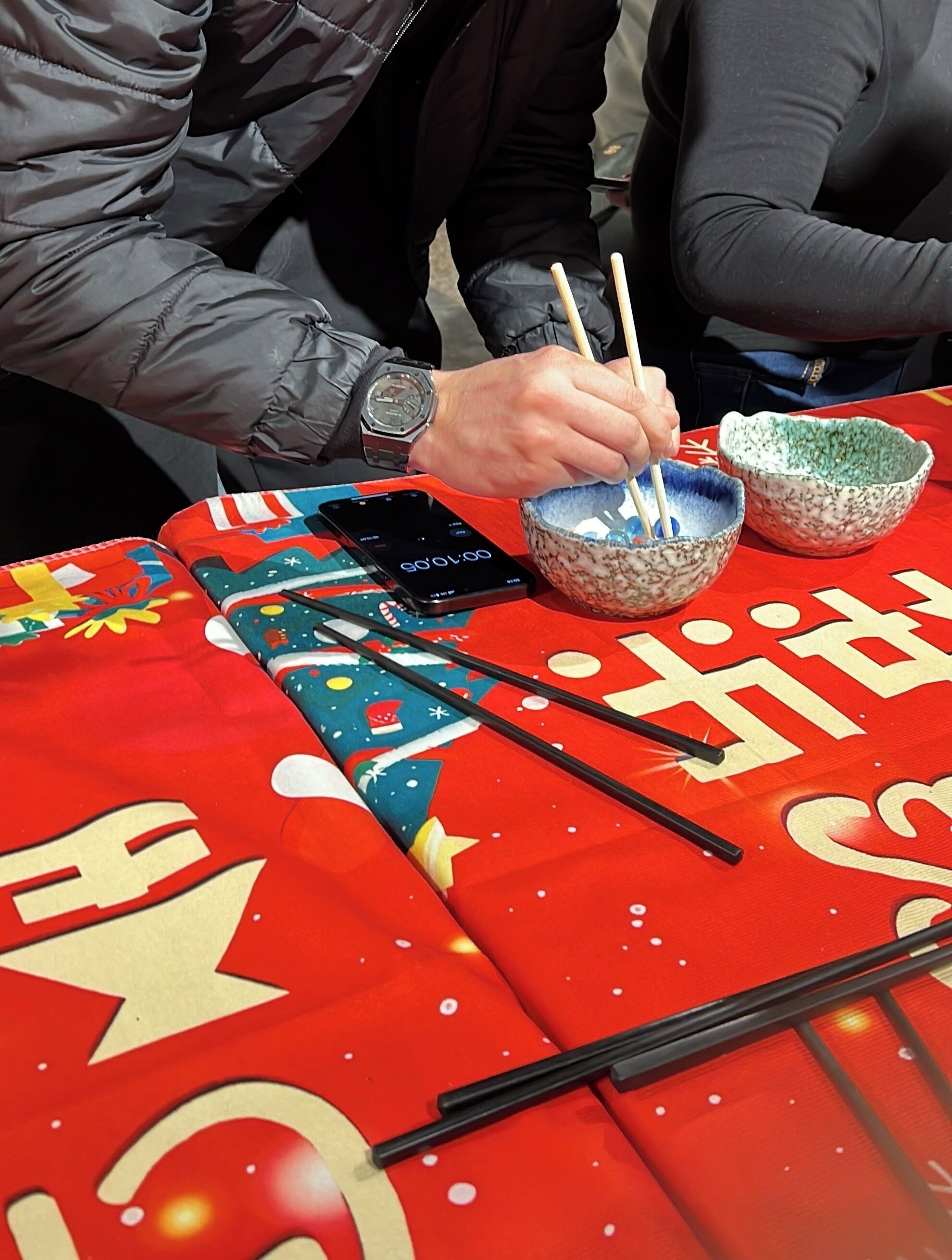 A table with a red tablecloth, chopsticks, a smartphone, and two bowls.