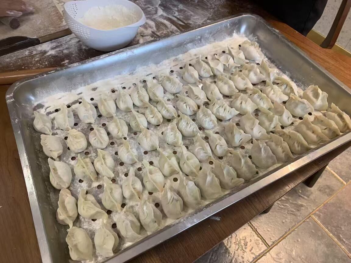 Une assiette de raviolis disposés sur une surface métallique, avec un bol de farine à proximité.