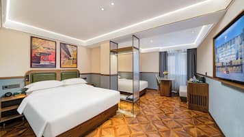 A hotel room with a large bed, a desk, a chair, a small table, and a TV.
