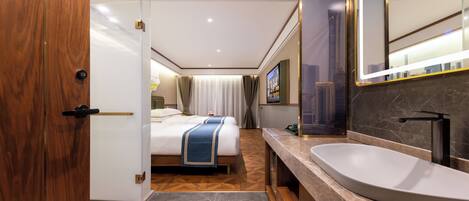 A modern hotel room with a large bed, a bathroom with a large sink and mirror, and a cityscape view.