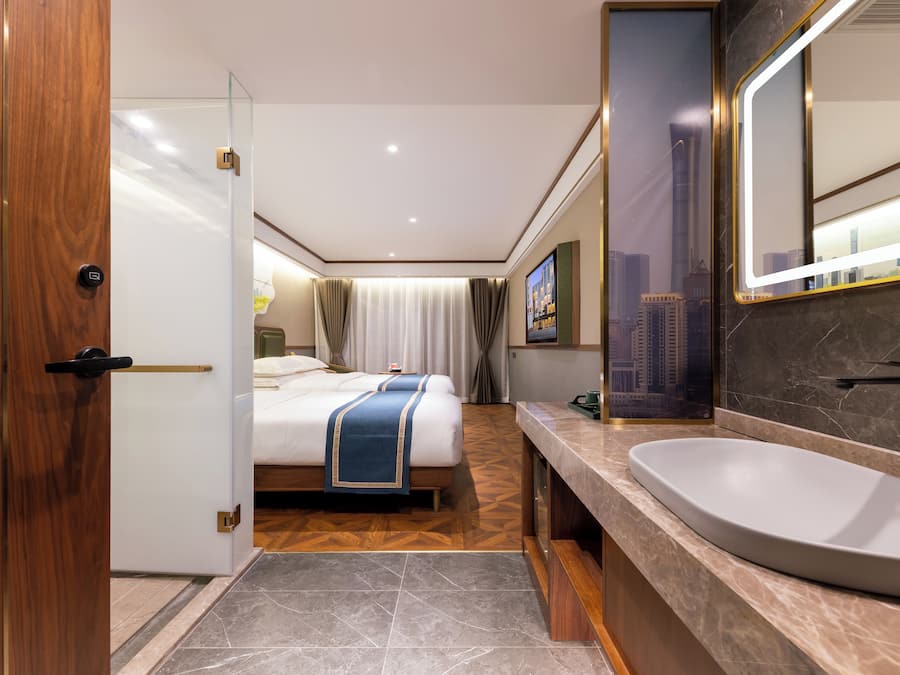 A modern hotel room with a large bed, a bathroom with a large sink and mirror, and a cityscape view.