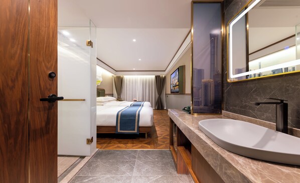 A modern hotel room with a large bed, a bathroom with a large sink and mirror, and a cityscape view.