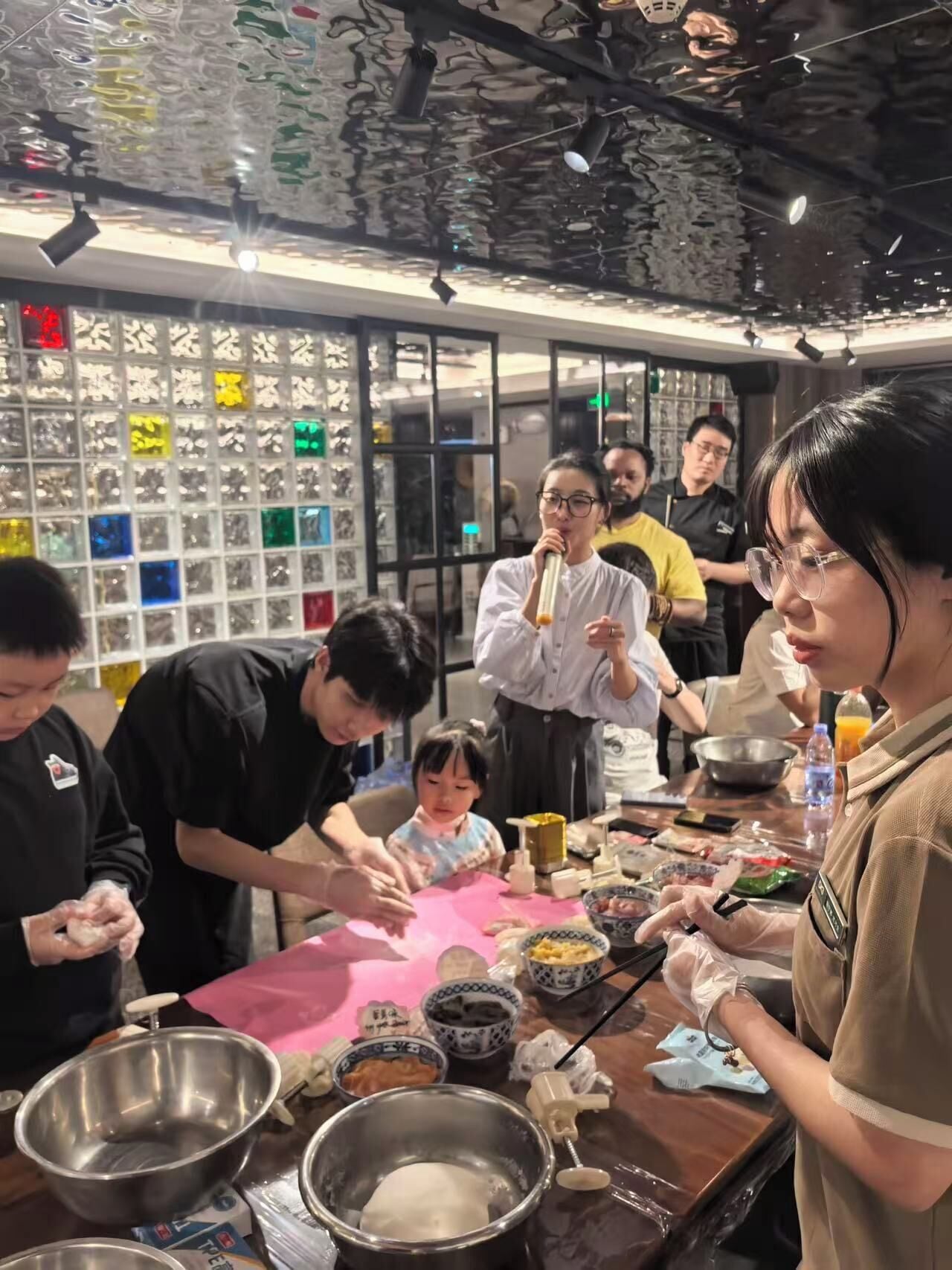 A group of people engaged in a cooking activity around a table with various cooking utensils and ingredients.