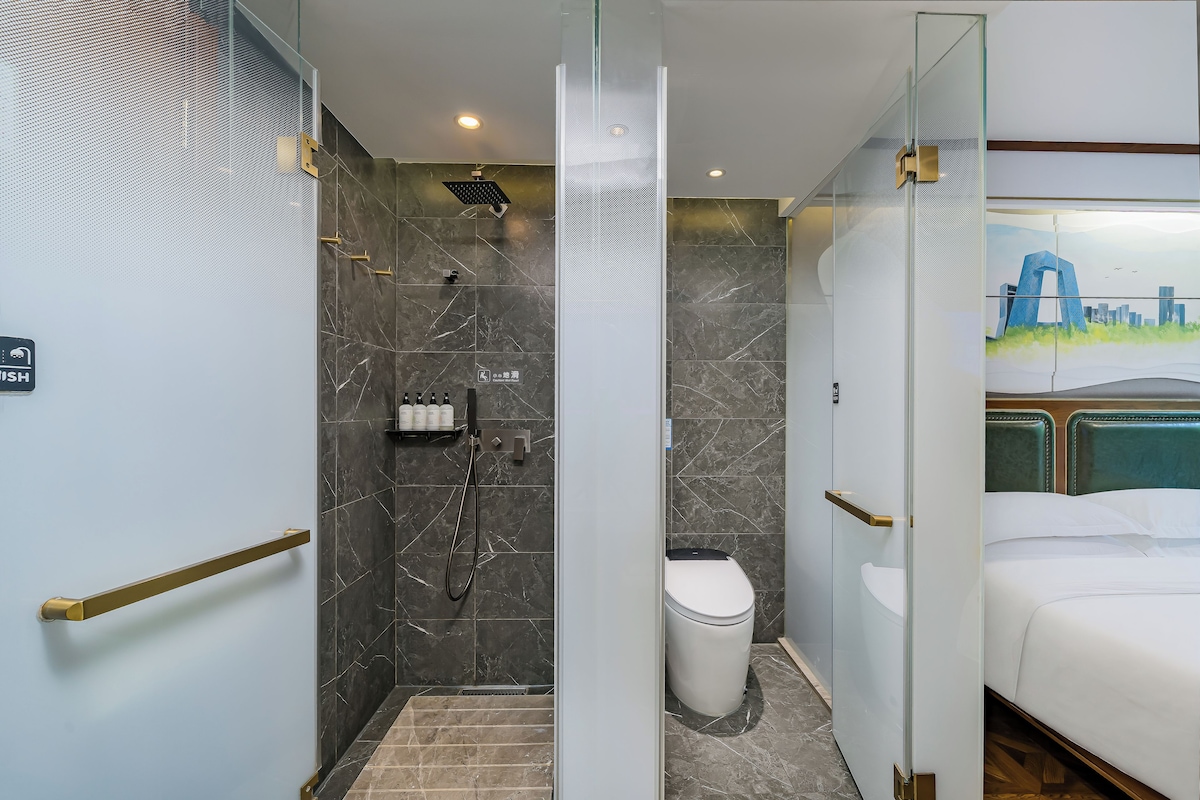A modern bathroom with a shower, toilet, and a bed with a cityscape view.