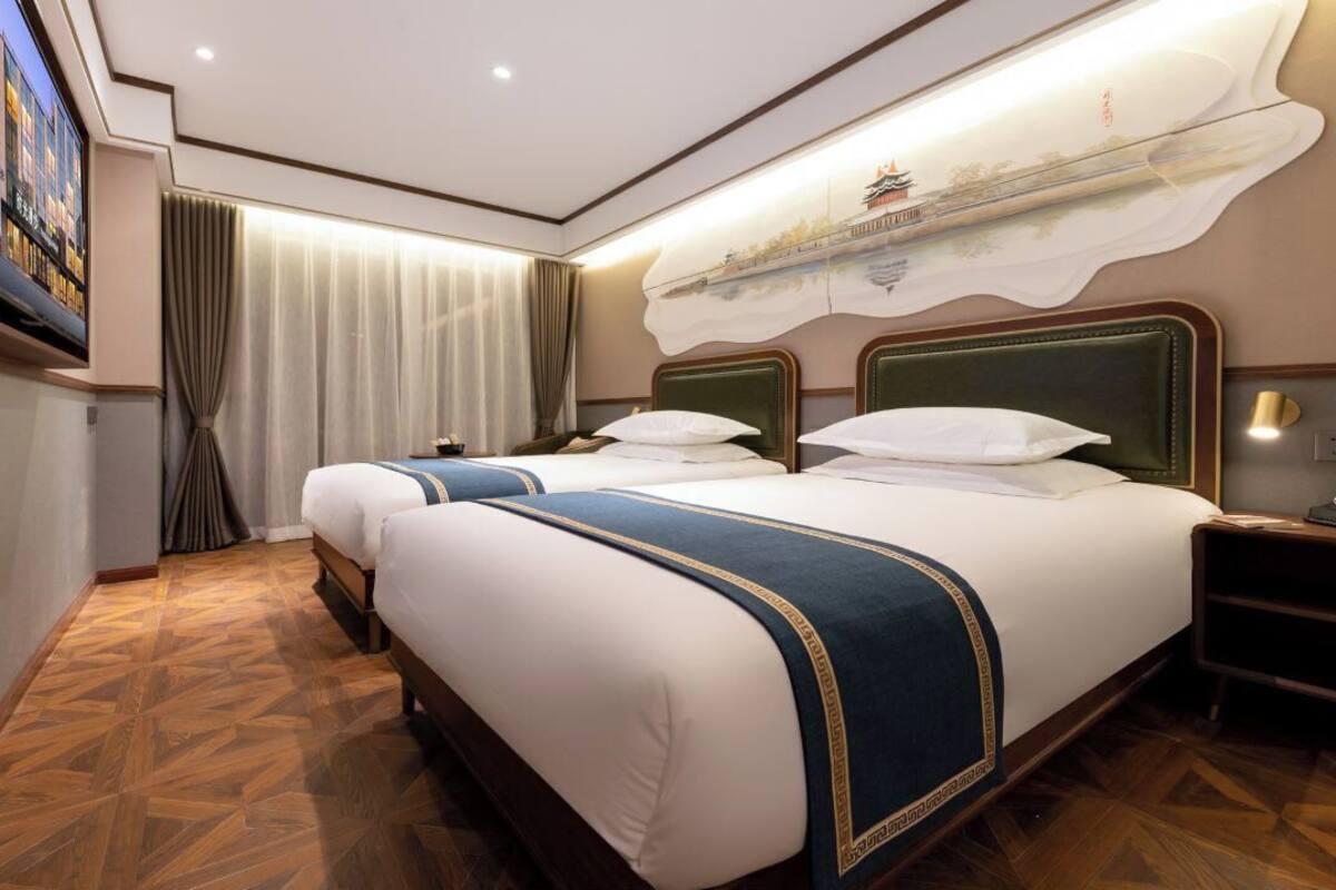Ein Hotelzimmer mit zwei Betten, einem Fernseher, einem Bild an der Wand und einem Holzboden.