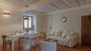 A cozy living room with a white sofa, a dining table with chairs, and a wooden door. - Lovely apartment for 4 guests with WIFI, A/C (Cortona)