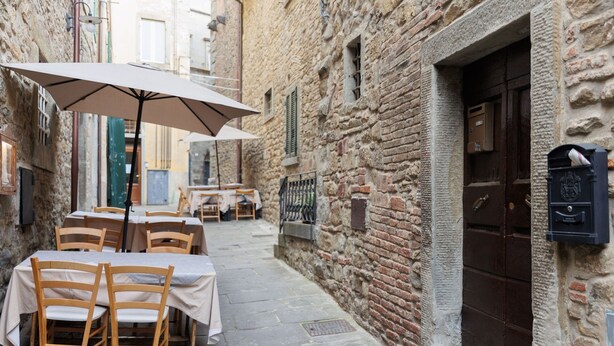 An outdoor café with tables and chairs, stone walls, and a mailbox. - Lovely apartment for 4 guests with WIFI, A/C (Cortona)