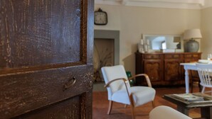 A room with a wooden door, a white chair, a wooden cabinet, and a table with a lamp. - Lovely apartment for 4 guests with WIFI, A/C (Cortona)