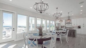 A spacious kitchen with white cabinetry, a dining area with a round table, and large windows offering a view of the ocean. - Beach Country 7 BR/ 7.5 House w/ Heated Pool (Navarre Beach)