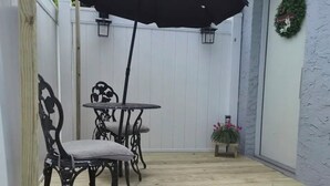 Une terrasse en bois avec une table et des chaises, un parasol noir et une lanterne.