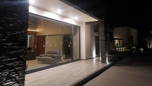 A modern house with a glass door entrance, a stone pillar, and a well-lit interior.