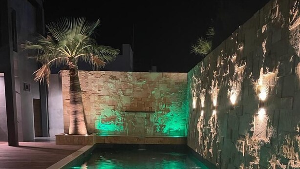 A swimming pool with clear water and a stone wall with lighting.