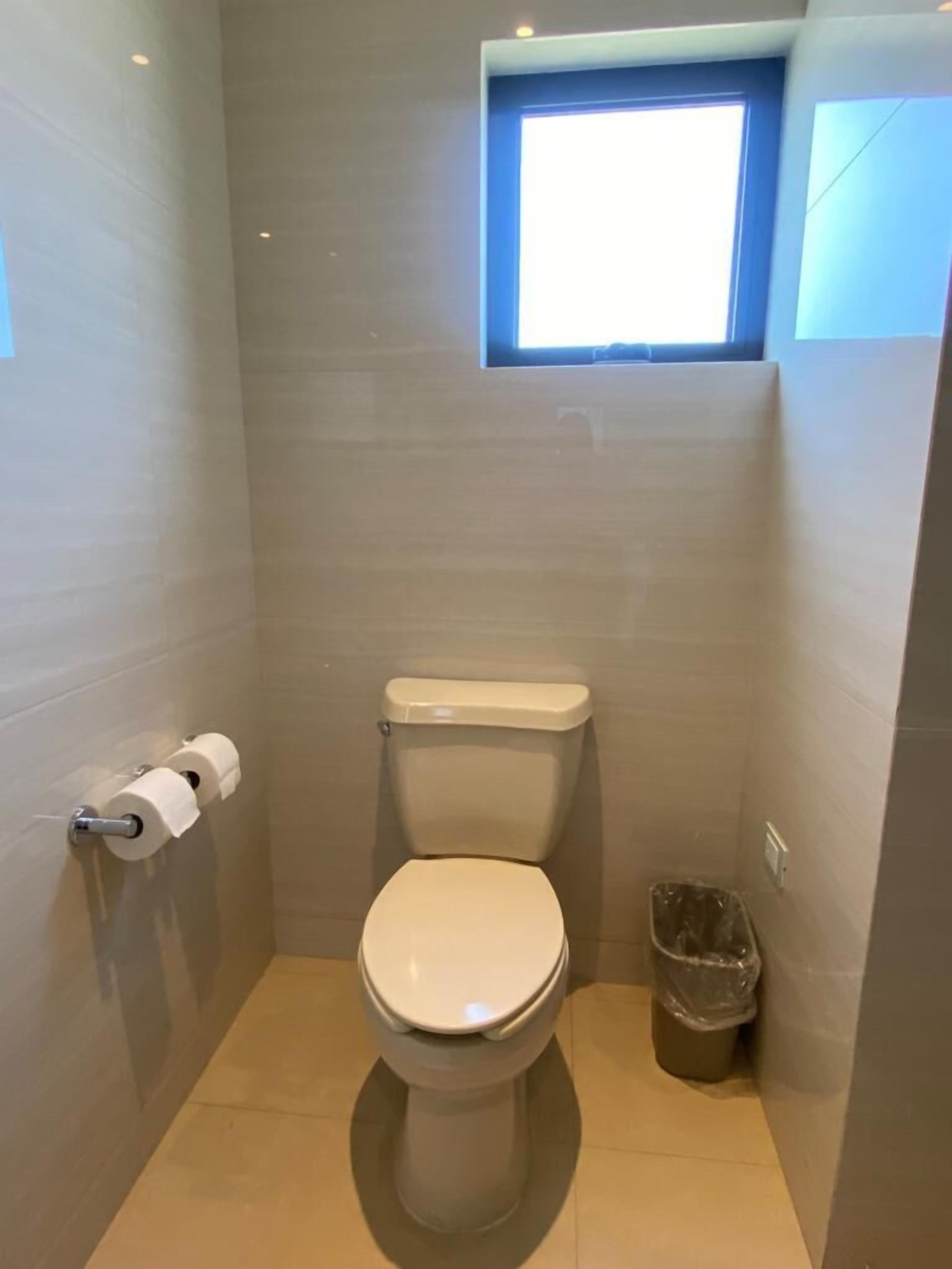 Un baño pequeño y moderno con inodoro, ventana y un cubo de basura.