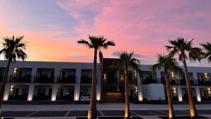 A hotel with multiple floors, a parking lot, and palm trees.