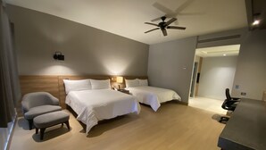 A hotel room with two beds, a desk, a chair, a ceiling fan, and a nightstand with a lamp.