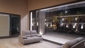 A modern living room with two sofas and a large glass wall offering a view of the street and palm trees.